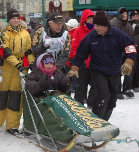 Jeff makes his way to the ceremonial start in Anchorage with Iditarider Elaine Strong all bundled up in the sled.
